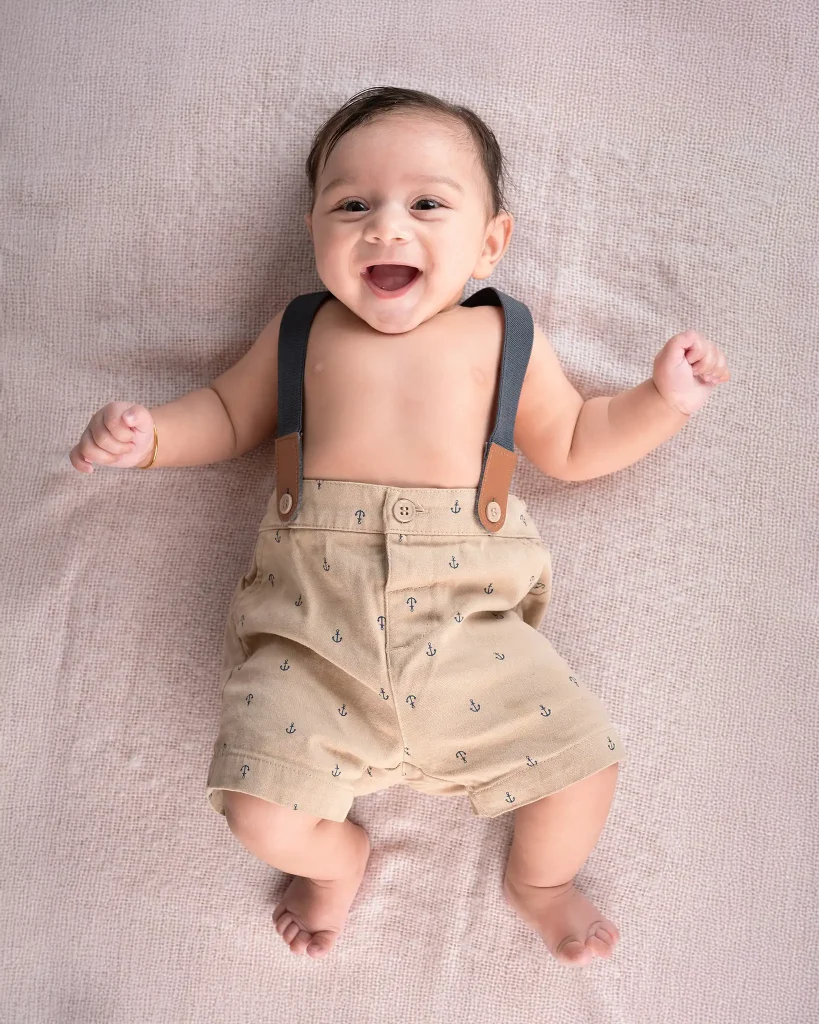 Laughing baby lying on a soft pink blanket wearing suspenders