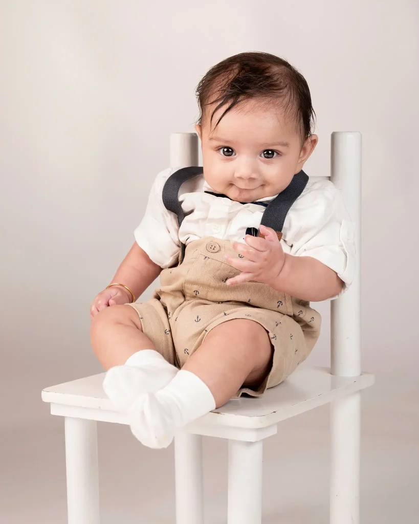 Studio baby portrait of a smiling infant sitting on a white chair