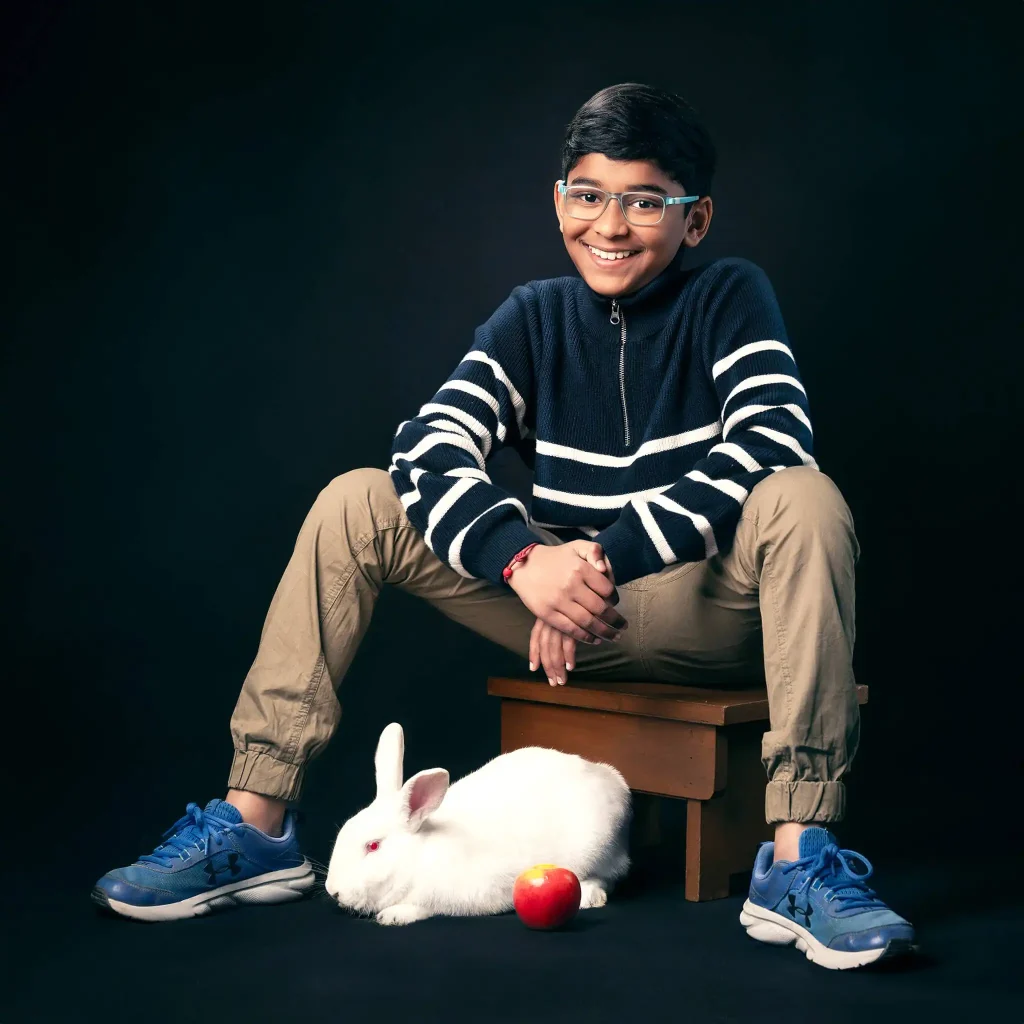 Happy boy seated with a white rabbit and apple in a studio portrait in Christchurch