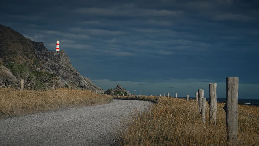 Scenic view of Cape Palliser Lighthouse from gravel coastal road in New Zealand