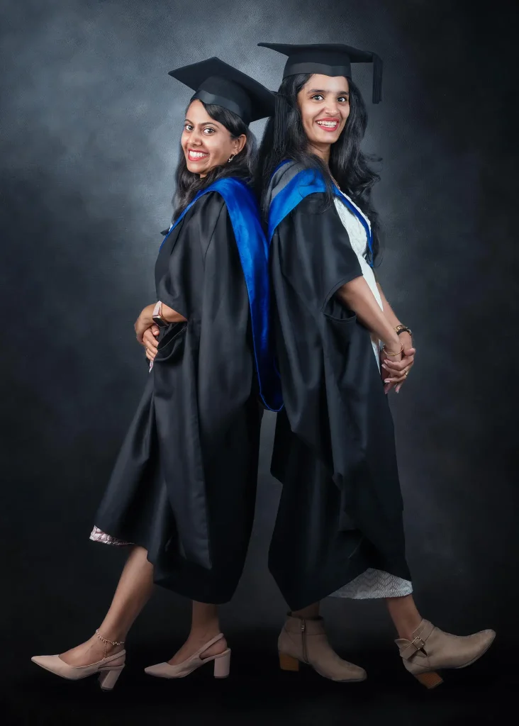 Two female graduates in academic gowns and caps posing back-to-back for graduation portrait