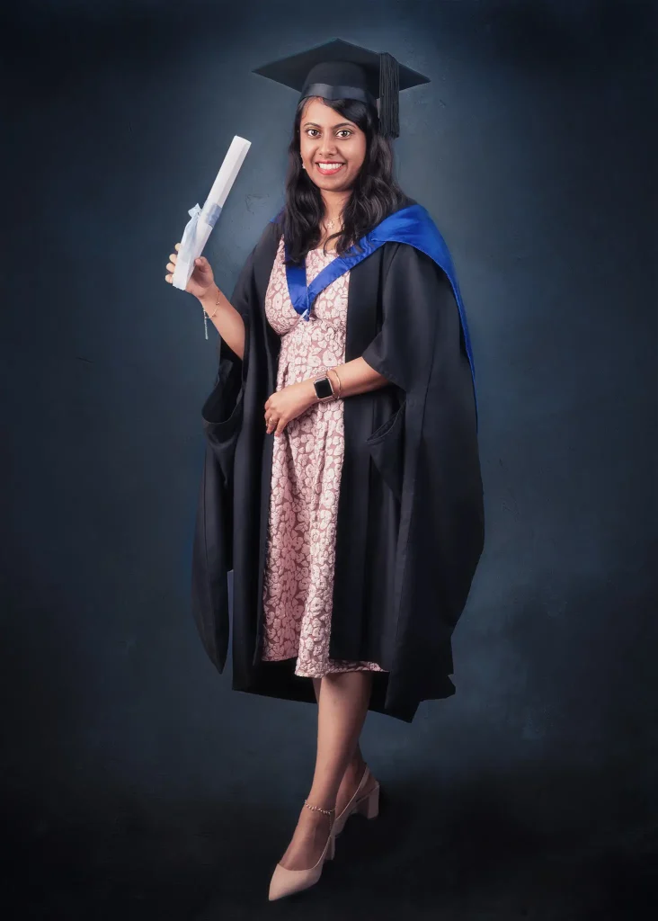 Female graduate in cap and gown holding diploma smiling for studio portrait
