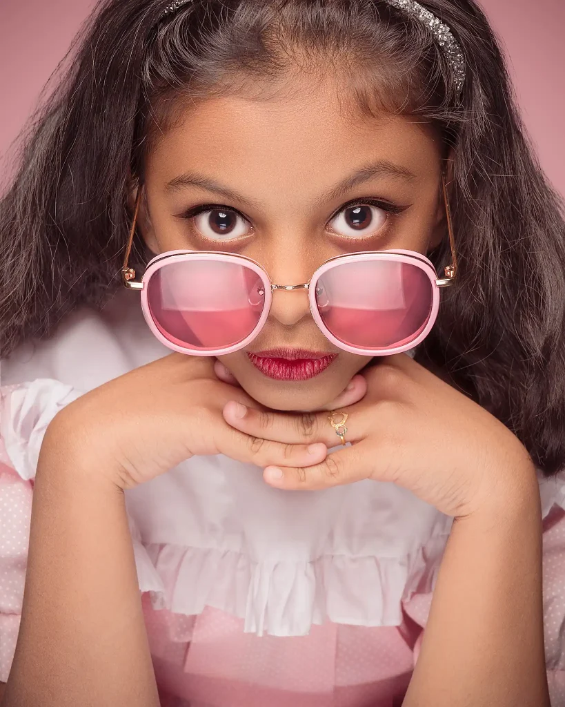Stylish portrait of young girl wearing pink sunglasses and white dress in Christchurch studio