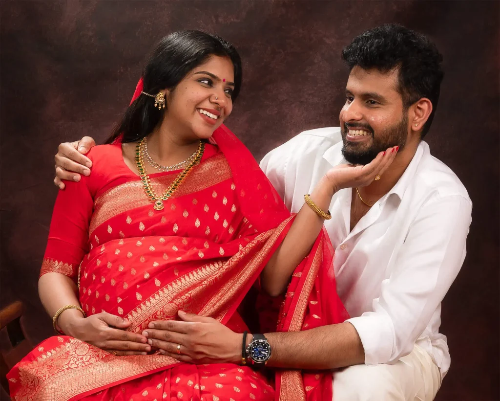 Indian couple smiling at each other, woman in red sari and man in white shirt in studio portrait