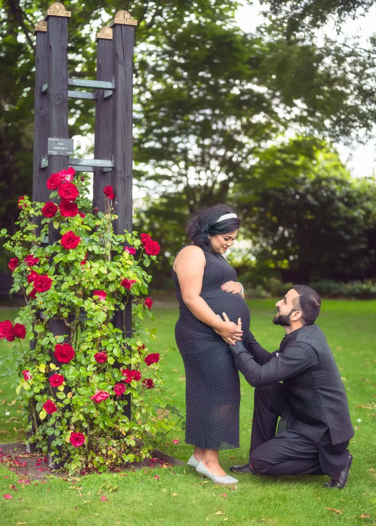 Christchurch maternity couple by rose trellis, husband kneeling at baby bump