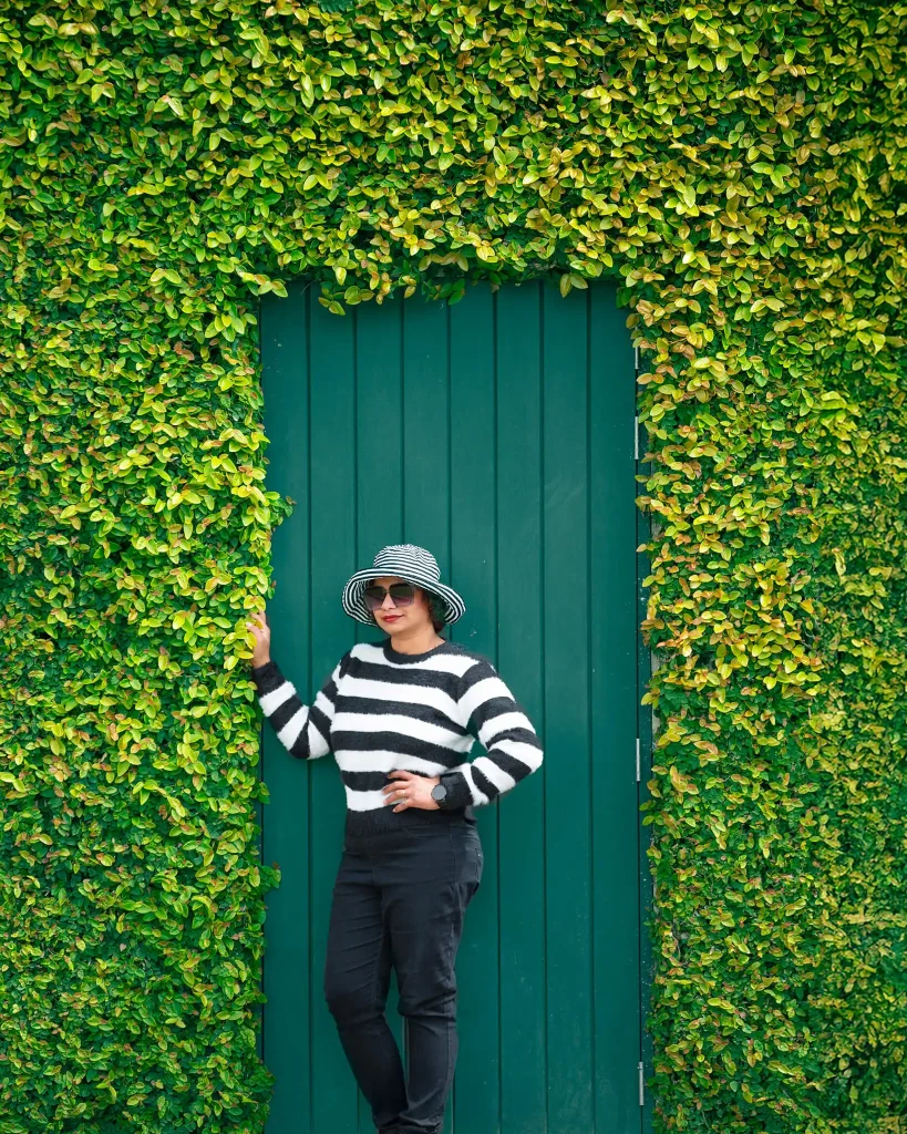 Woman in striped sweater posing by a green ivy-covered wall at Hamilton Gardens