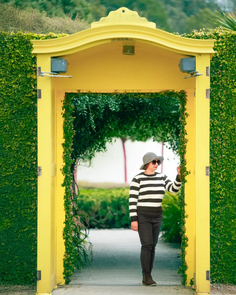 Woman walking under a vibrant yellow archway surrounded by greenery at Hamilton Gardens