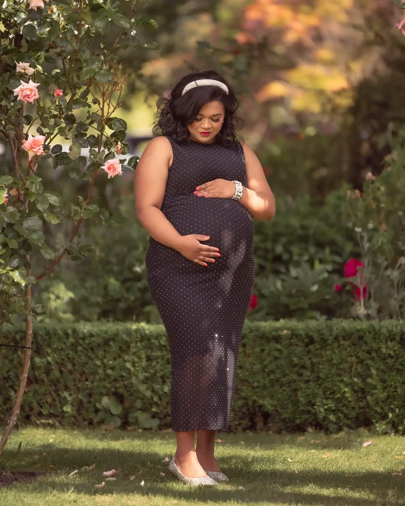 Pregnant woman in a black polka-dot dress walking through a garden, full-body maternity portrait