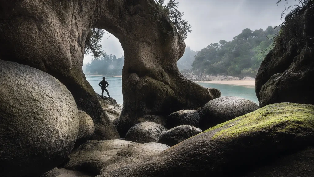 Man standing near rock arch at the Split Rock in New Zealand