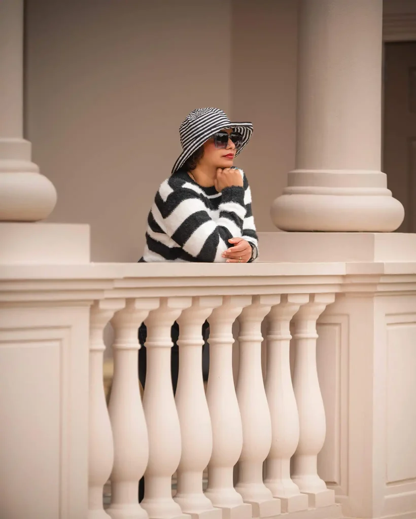 Woman in striped sweater and hat leaning on a pale architectural balcony with columns in Hamilton Gardens